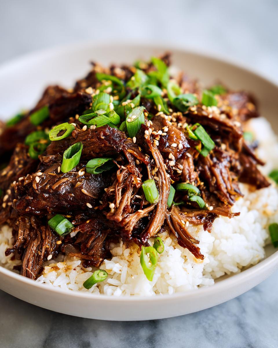 Close-up of Slow Roast Asian Beef served over rice, garnished with sesame seeds and green onions.