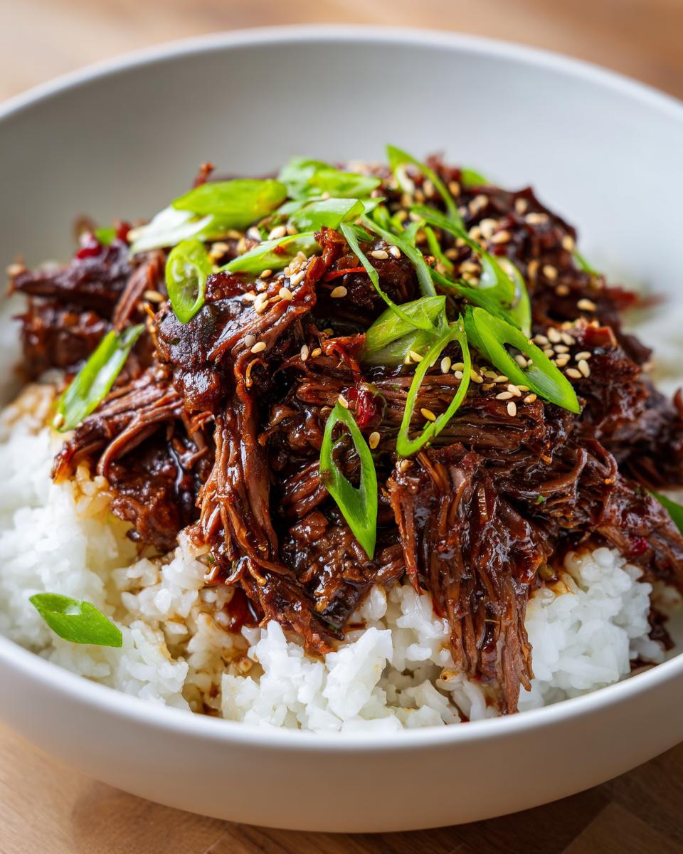 A bowl of Slow Roast Asian Beef served over white rice, garnished with green onions and sesame seeds.