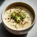 A bowl of creamy Spicy Jalapeño Popper Soup topped with sliced jalapeños and spices.