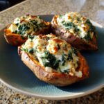 Three Stuffed Sweet Potatoes with Spinach and cheese filling on a blue plate, ready to eat.