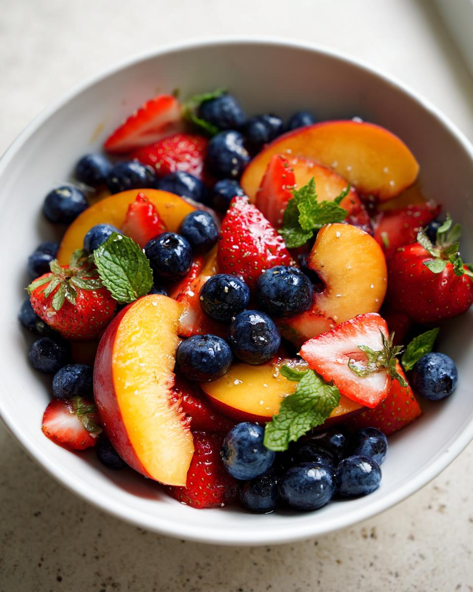 A vibrant bowl of Summer Peach Fruit Salad featuring peaches, blueberries, and strawberries, garnished with mint.