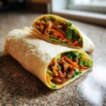 Two Sweet Chili Chicken Wraps, one cut in half, showcasing the chicken, lettuce, and carrots filling.