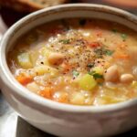 A comforting bowl of White Bean Soup, showcasing beans, vegetables, and a sprinkle of pepper.