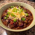 A bowl of hearty 5-Ingredient Ground Beef chili topped with shredded cheese and green onions.