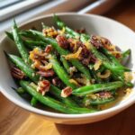 A bowl of 5-Ingredient Thanksgiving Green Beans, topped with pecans and fried onions.