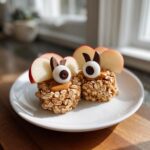 Two Apple Monster Bites on a white plate, featuring oats, peanut butter, apple slices, candy eyes and chocolate.