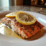 A delicious Bake-From-Frozen Salmon fillet, seasoned and topped with lemon slices on a white plate.