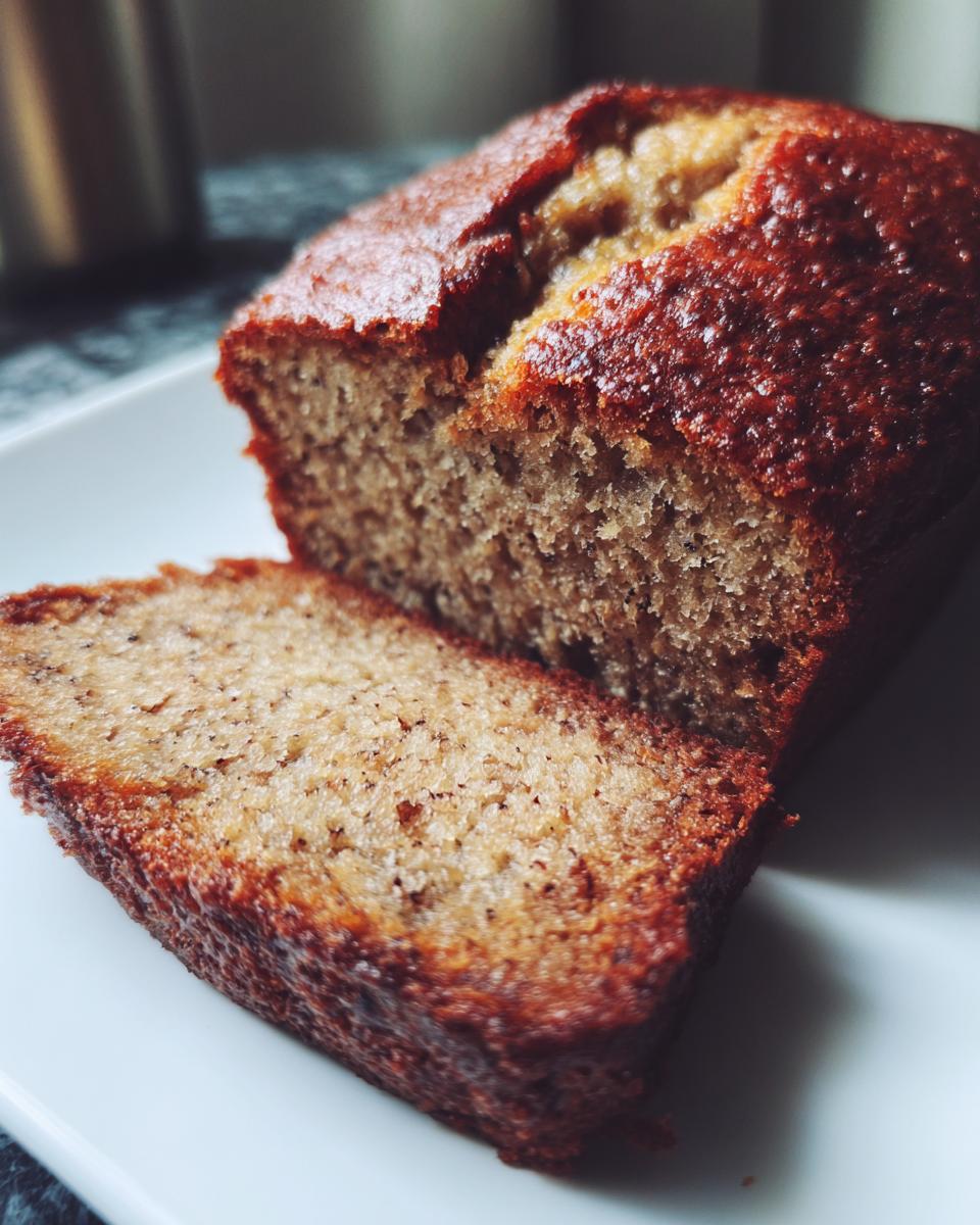 A loaf of Banana Bread with a slice cut, showcasing its moist texture. Perfect for busy weeknights.