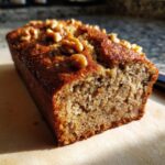 Close-up of a loaf of Banana Bread Recipe Everyone Asks For, topped with walnuts, on a wooden board.