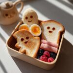 A Bento-Style Spooky Breakfast Box with ghost-shaped toast, rice ball, eggs, berries, and ham.