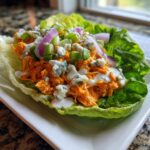 A delicious Buffalo Chicken Lettuce Wraps on a plate, topped with blue cheese, scallions and red onions.