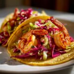 Two Cajun Shrimp Tacos With Slaw on a white plate, featuring seasoned shrimp and colorful slaw.