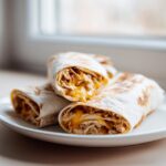 Three Ooey-Gooey Cheesy Garlic Chicken Wraps on a white plate, showing melted cheese and chicken filling.