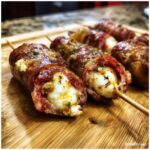 Close-up of Creepy Skewered Salami “Eyeballs” on a wooden board, featuring salami wrapped around cheese balls on skewers.