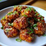 A plate of glistening Honey Garlic Chicken Bites, sprinkled with sesame seeds and green onions.
