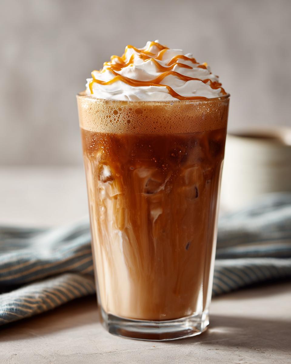 Iced Starbucks drink topped with whipped cream and caramel drizzle, perfect for learning how to make Starbucks drinks.