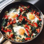 A skillet featuring a vibrant One-Pan Breakfast Idea with eggs, spinach, and red bell peppers.