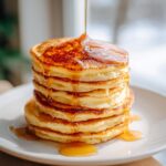 A stack of Protein Ghost Pancakes being drizzled with syrup on a white plate.