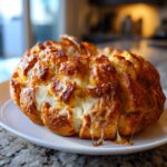 Golden Pumpkin-Shaped Cheesy Pull-Apart Bread with melted cheese on a white plate.