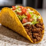 Close-up of a Restaurant-Style Ground Beef taco with lettuce and tomatoes in a crispy shell.