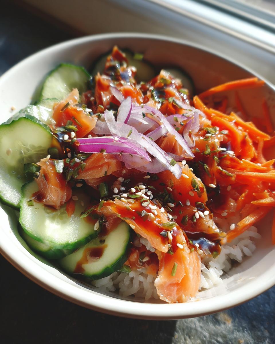 Close-up of a Salmon Bowl with rice, salmon, cucumbers, carrots, and red onions, drizzled with sauce and sesame seeds.