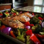 Sheet-Pan Salmon & Veggies on a baking sheet, featuring salmon fillets, broccoli, red peppers, and red onions.