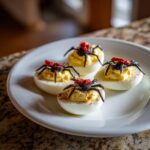 Four Spider Deviled Eggs on a white plate, decorated with spider and paprika.