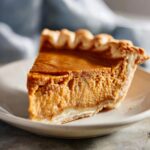 A slice of pumpkin pie, a perfect Thanksgiving Desserts option, on a plate with a flaky crust.