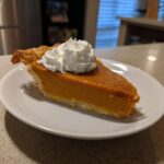 A slice of pie, a Thanksgiving Desserts Recipe, topped with whipped cream on a white plate.