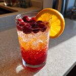 A colorful Thanksgiving drink with cranberries, orange slice, and sparkling liquid. One of the Best Thanksgiving Drinks 2025.