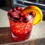 A refreshing Thanksgiving Drinks in 20 Minutes cocktail with cranberries and an orange slice.