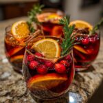 Glasses of Thanksgiving Drinks garnished with cranberries, orange slices, and rosemary sprigs.
