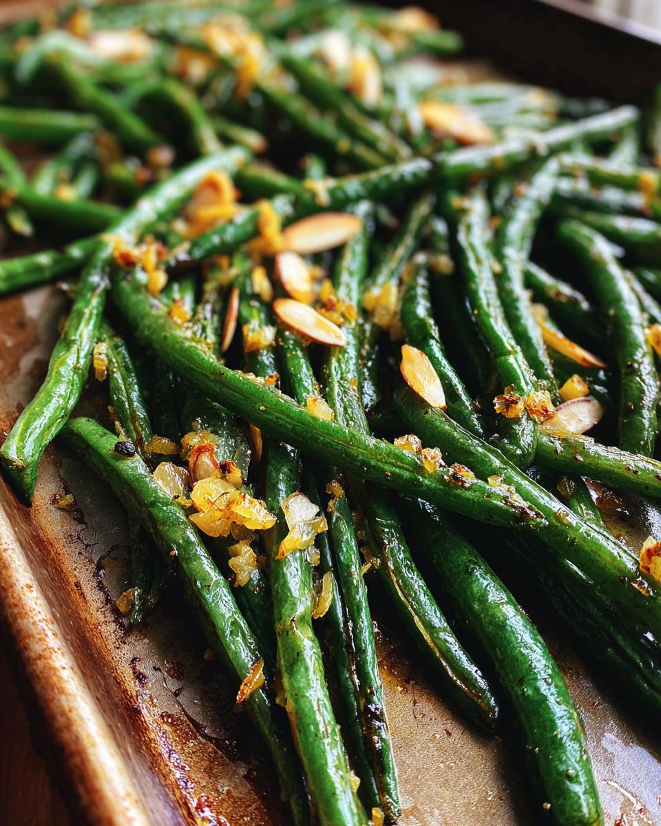 Close-up of Thanksgiving green beans on a baking sheet, topped with toasted almonds and caramelized onions.