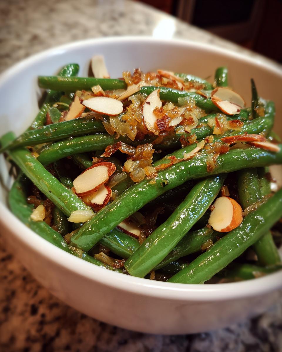 Close-up of Thanksgiving green beans in a white bowl, topped with toasted almonds and caramelized onions.