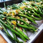 Close-up of Thanksgiving Green Beans topped with toasted almonds and caramelized onions on a metal sheet pan.