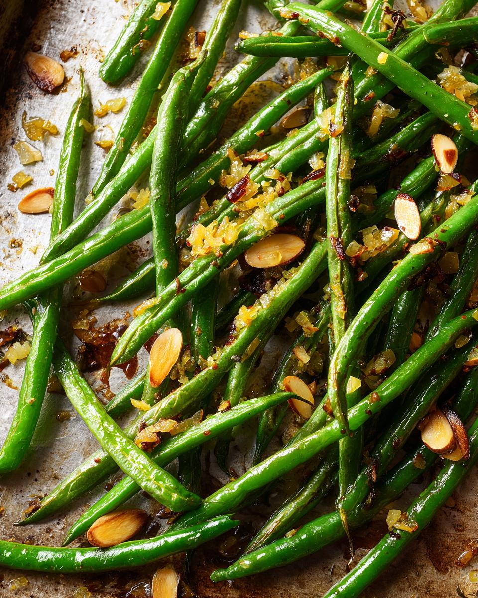 Overhead shot of Thanksgiving green beans with toasted almonds and caramelized onions on a baking sheet.