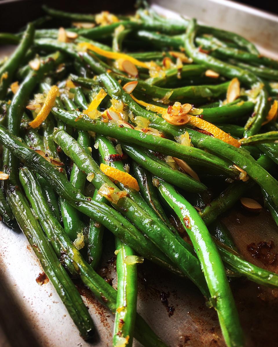Close-up of Thanksgiving green beans with lemon zest and sliced almonds on a baking sheet.
