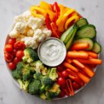 Colorful Thanksgiving veggie tray with broccoli, cauliflower, carrots, peppers, tomatoes, cucumbers, and dip.