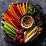 Overhead shot of a colorful Thanksgiving veggie tray with carrots, celery, broccoli, radishes, and hummus.