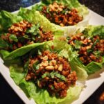 Close-up of four Turkey Lettuce Wraps (PF-Style) on a white plate, garnished with peanuts and cilantro.