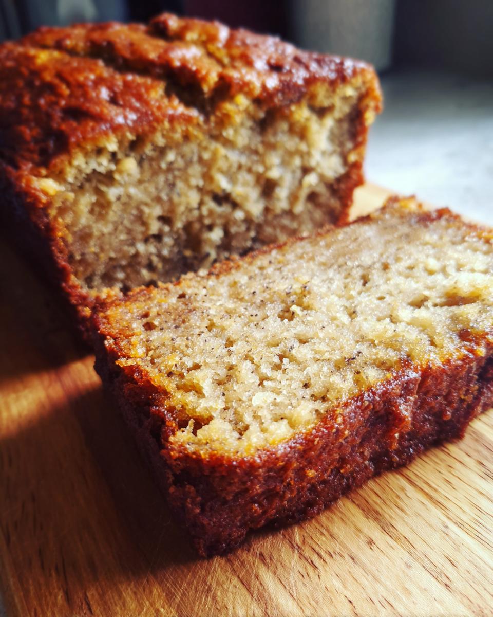 Close-up of a slice of Ultimate Banana Bread on a wooden cutting board, showcasing its moist texture.