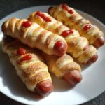 A plate of Whole-Wheat Mummy Dogs, baked and topped with ketchup 'eyes'.