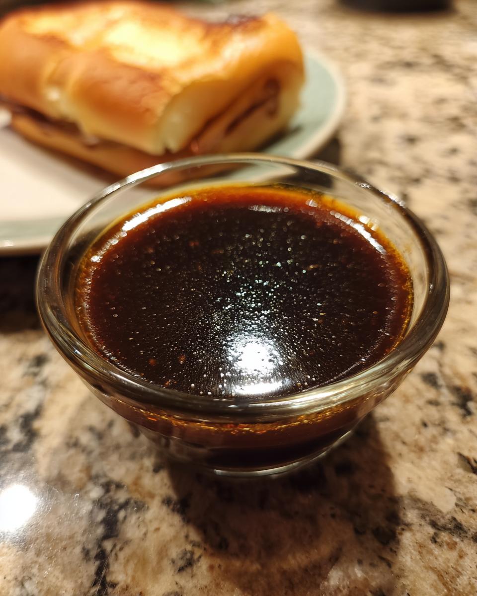 A small glass bowl filled with rich, dark Au Jus sauce, perfect for dipping French Dip Sandwiches.