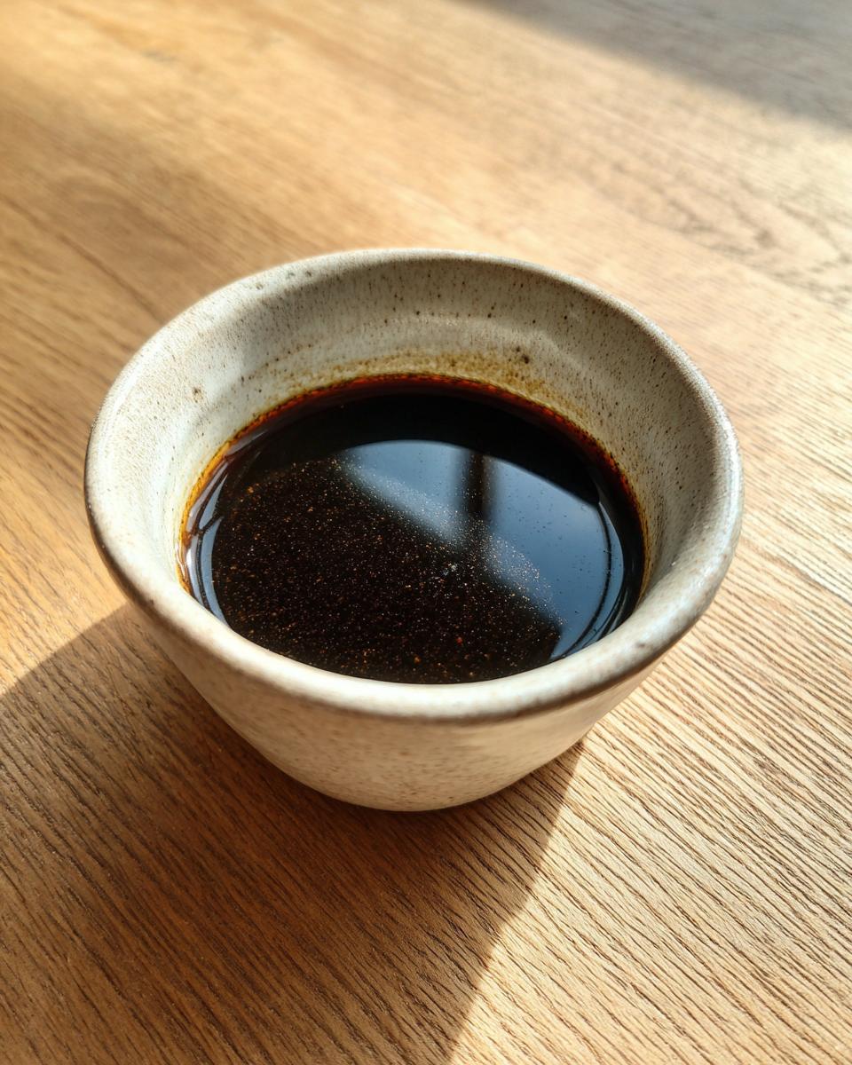 A close-up of a rustic bowl filled with rich, dark homemade au jus, perfect for the Best Homemade Au Jus Recipe.