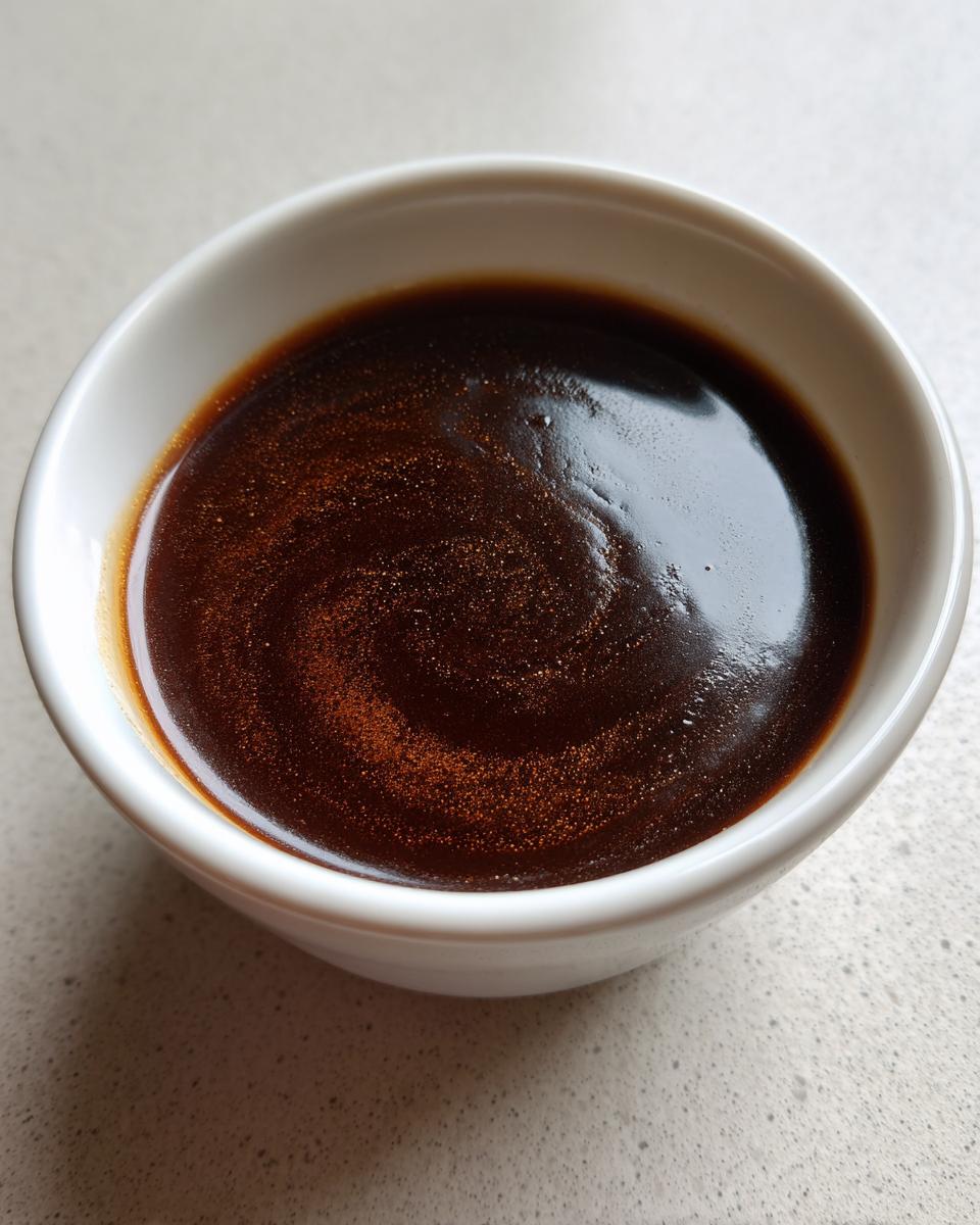 A close-up of a white bowl filled with rich and flavorful beef au jus, showing a swirling pattern.