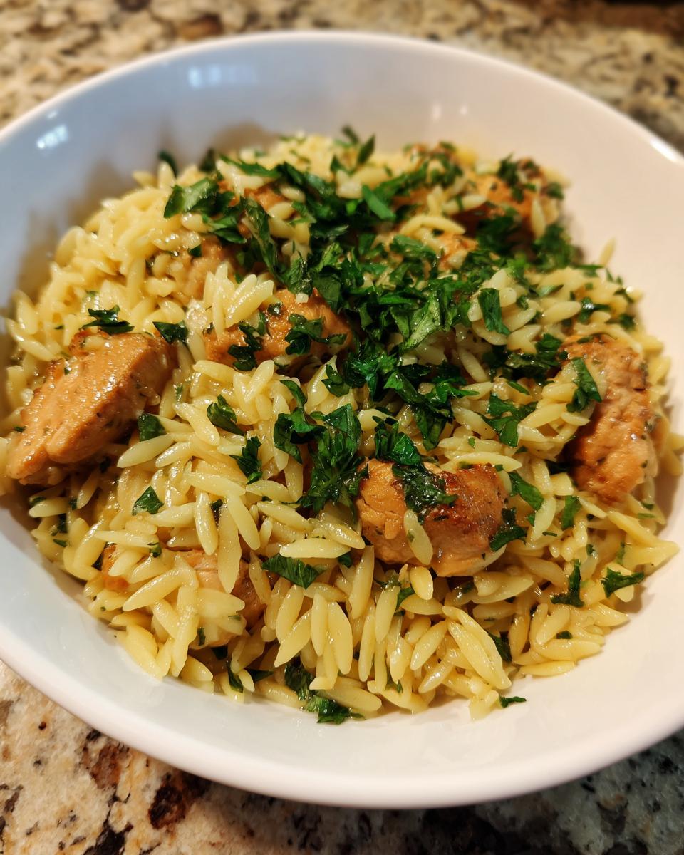 Close-up of a white bowl filled with the Best Orzo Dinner Recipe for Busy Moms, featuring chicken pieces and fresh parsley.