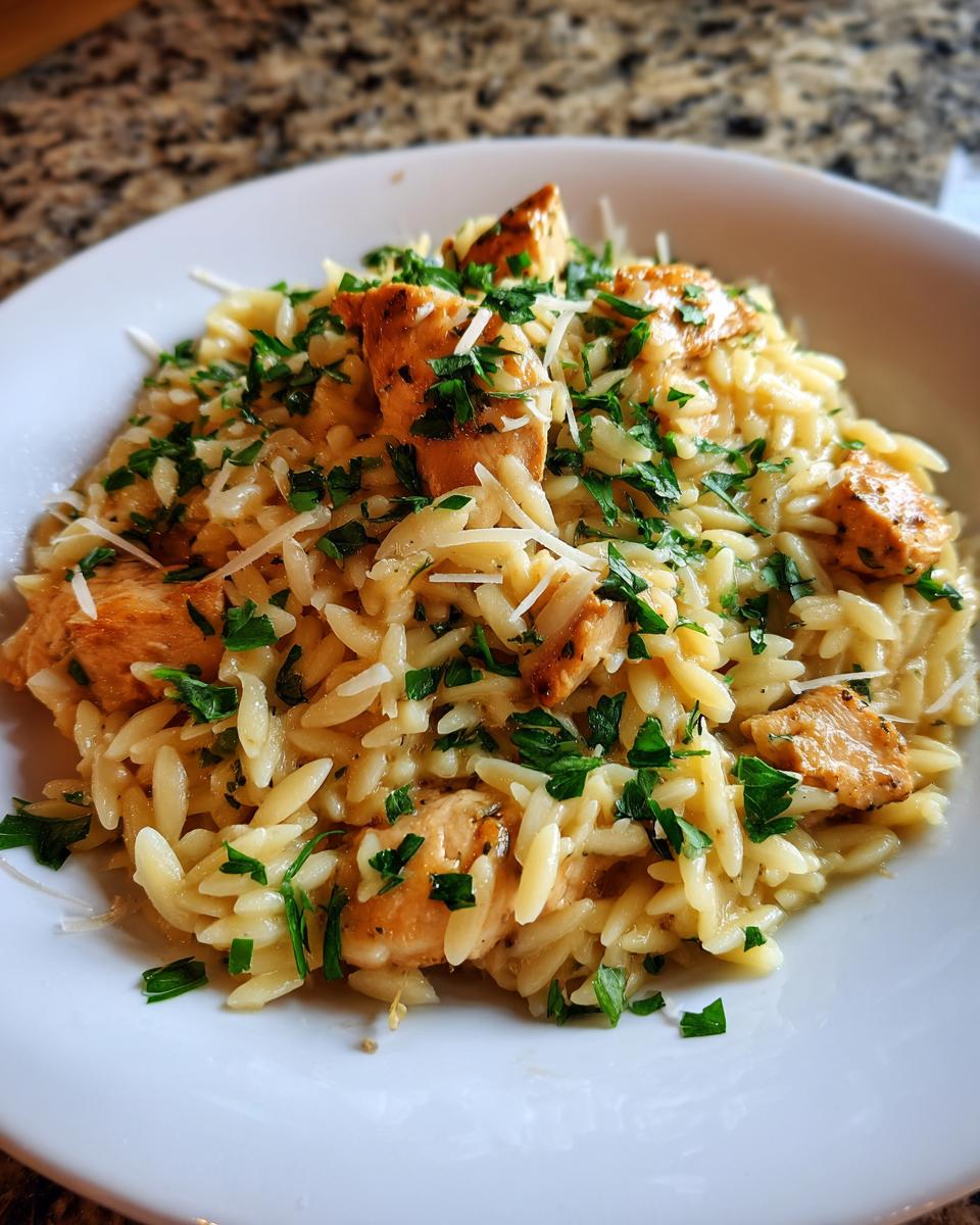 Close-up of a white bowl filled with the Best Orzo Dinner Recipe for Busy Moms, topped with chicken pieces and fresh parsley.