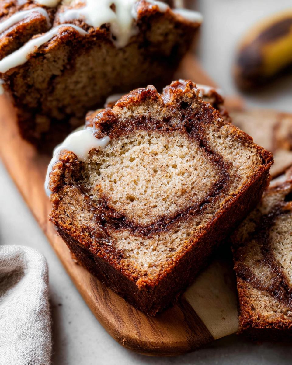 Close-up of a thick slice of Cinnamon Swirl Banana Bread showing the rich cinnamon swirl and white glaze.