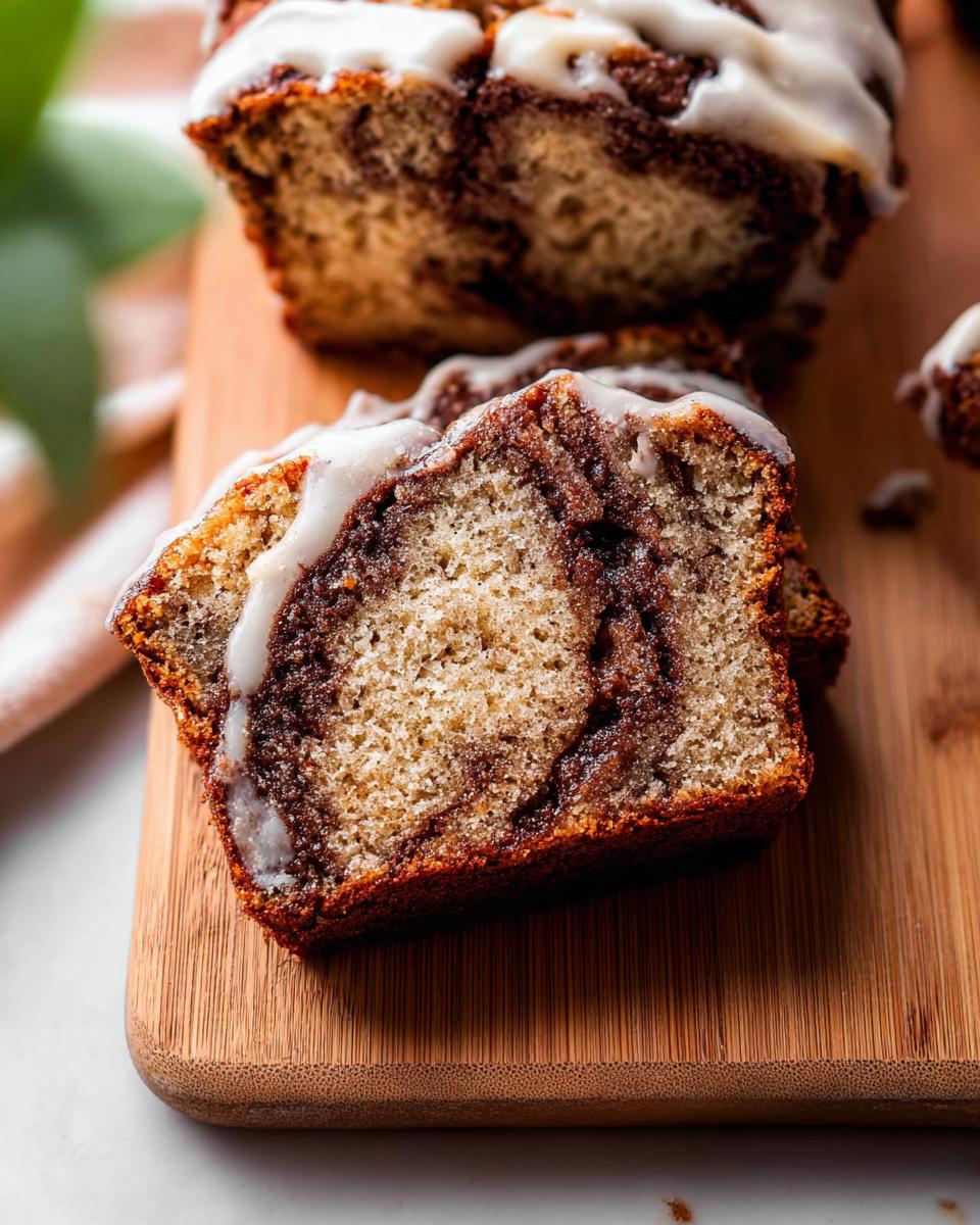 Close-up of a moist slice of Cinnamon Swirl Banana Bread showing the dark cinnamon ribbon and white vanilla glaze.