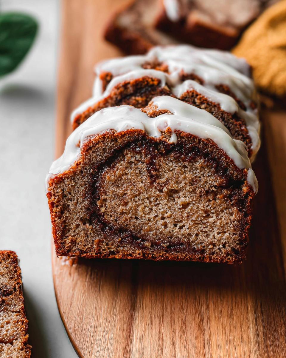 Close-up of sliced Cinnamon Swirl Banana Bread topped with white glaze on a wooden board.